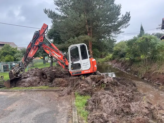 Bagr v korytě mezi silnicí a zástavbou